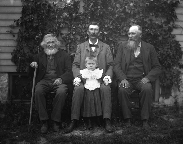 Outdoor group portrait of four generations of three Krueger men and one boy. Sitting left to right are: William (holding cane), Alexander and August Krueger. Edgar Krueger is standing in the middle, between his father's legs.