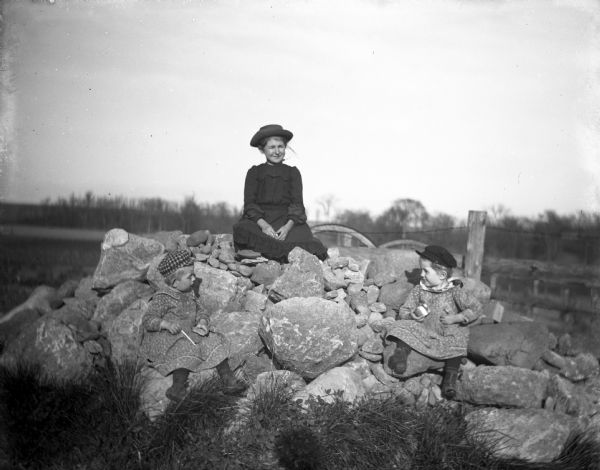 Jennie and Edgar Krueger playing with Effy Goetsch Carr on a pile of rocks. All three children have toys in their hands.