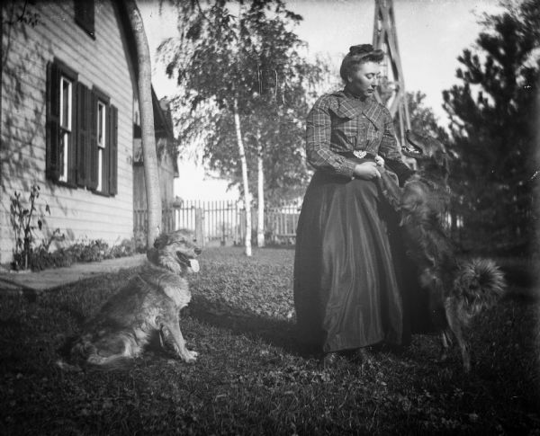 Sarah Krueger playing with two dogs, Sailor and Pup, in the yard. One dog is jumping up to her while the other is sitting nearby.