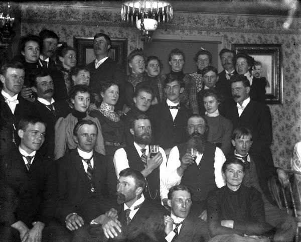 Indoor group portrait of neighbors who gathered together for a party at the Reibe's house. Alexander Krueger is sitting in the front on the left, with his wife, Florentina (third from left), and his sister, Sarah (fifth from left).