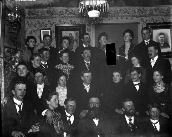 Indoor group portrait of several neighbors who gathered together for a party at the Reibe House. Sarah Krueger is third from the right in the back row. Her sister-in-law, Florentina Krueger, is sitting in the front row on the left.