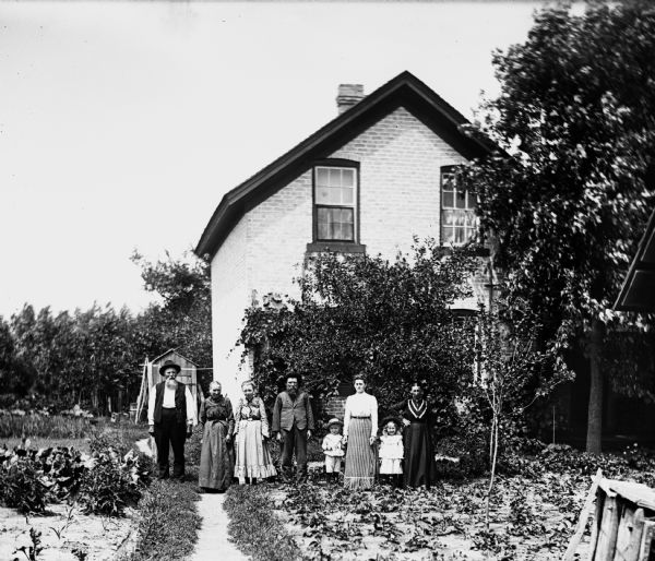 Members of the Krueger and Ullrich families standing in a garden located at the front of the Ullrich home. August is standing on the far left, while Edgar, Florentina, Jennie, and Mary are standing on the right.