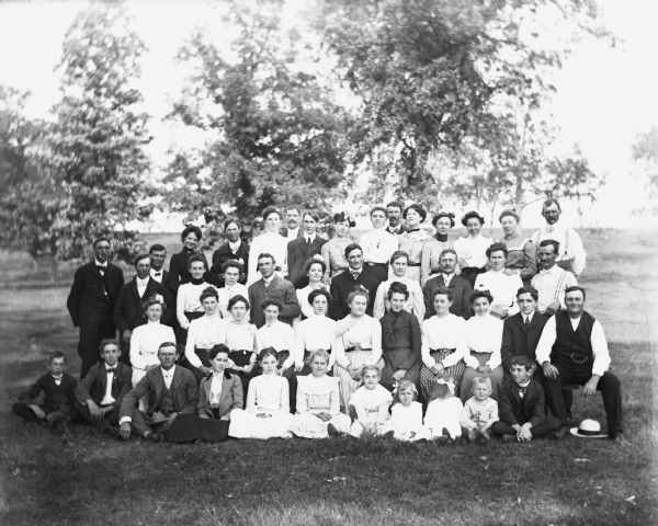Large group portrait of people attending a picnic in the Wills family woods. Flora and Hattie Fels are sitting fifth and sixth from the right in the front row, while Jennie and Edgar are sitting second and third. George (first on right) and Ida Fels (sixth from right) and Florentina (fourth from right) are sitingt in the second row. Sarah Krueger is standing second from right in the back row.