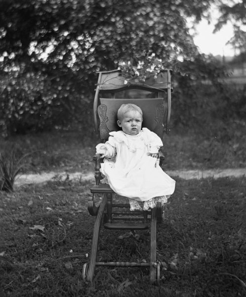 Outdoor portrait of infant Dorothy Goetsch sitting in a highchair. Ivy and branches are fastened to the top of the chair.