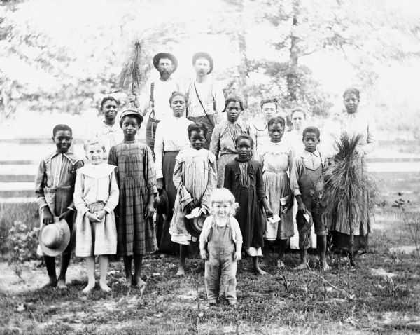 A group portrait of strawberry pickers who work at Paul C. Goetsch's farm. Ernst Goetsch and Alexander Krueger are standing elevated behind the pickers. Paul Goetsh's son, Russel Goetsh, is standing in front of the group.