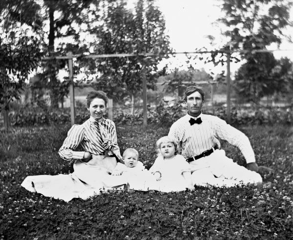 Outdoor group portrait of Paul C. Goetsch, his wife, and two children, Dorothy and Russel. They are sitting on the lawn in a patch of clover.