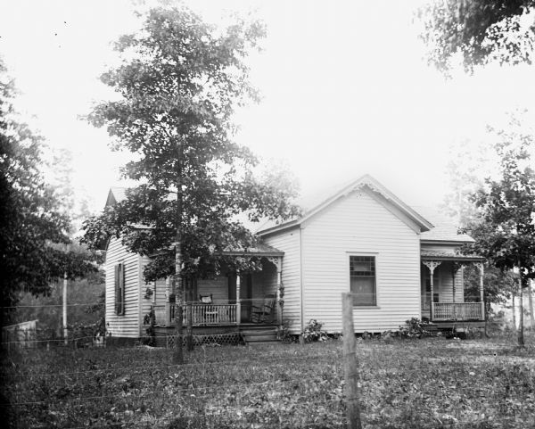 Home of Mr. Dake in Shelby County. There are two porches, one on the left and one on the right. Several trees are in the fenced-in front yard.