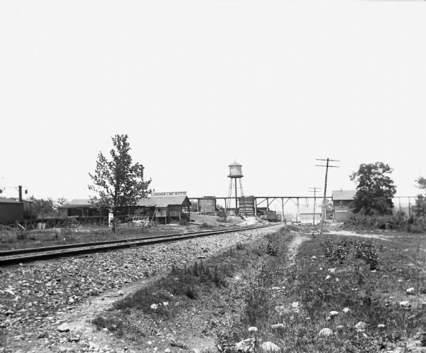 View across railroad tracks that lead to the main town, where the Longview Lime Works, sawmill, post office, general store, and telegraph station are located. Further down the tracks, elevated tracks are crossing over near the water tower.