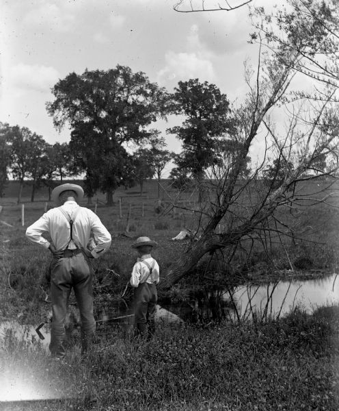 Alexander and Edgar Krueger fishing along a small creek on their farm. Both have their backs to the camera, looking into the water below.