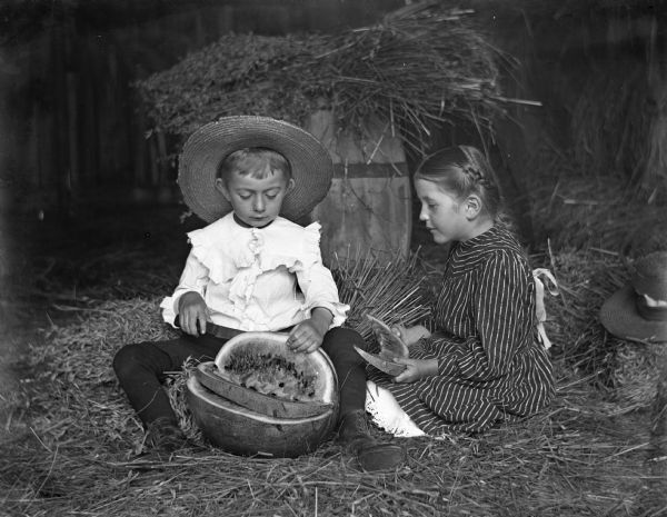 Jennie and Edgar Krueger sitting in hay barn, cutting up and eating a watermelon.