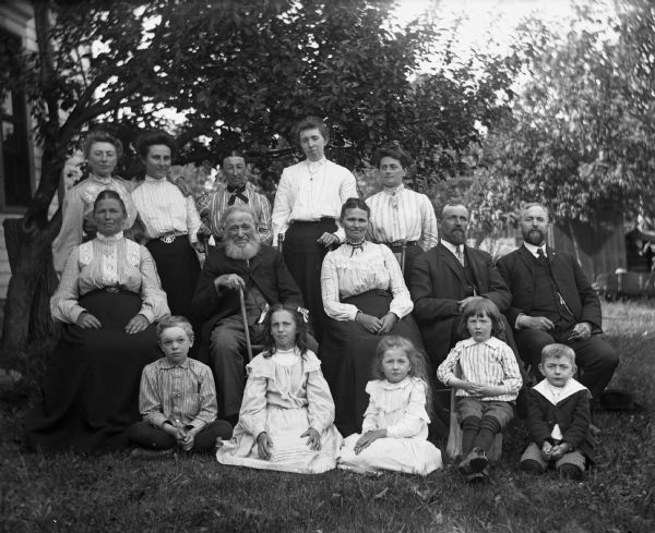 Outdoor portrait of the Krueger family posing in the yard with members of the Kraus and Goetsch families. Featured are Sarah, Mary, Florentina, William, Minnie, Albert, Henry, Rexford, Jennie and Edgar Krueger and Bertha Krueger Goetsch.