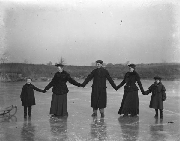 Edgar Krueger, Sarah Krueger, Ernie Buelke, Florentina Krueger, and Jennie Krueger holding hands on the iced over quarry pond.  A sled is on the ice near Edgar.