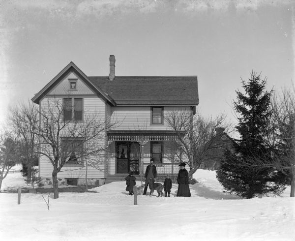 Alexander, Florentina, Jennie, and Edgar Krueger standing in front of their home with two of their dogs during winter. A barn is in the background on the right.