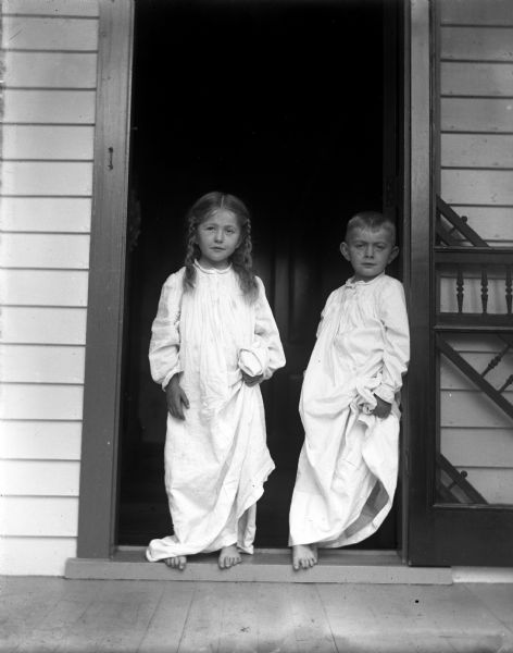 Jennie and Edgar Krueger standing barefoot in the front doorway wearing their nightgowns.