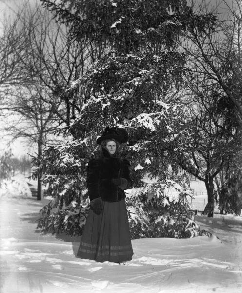 Outdoor portrait of Florentina Krueger wearing a fur coat while standing in front of a snow-covered pine tree.