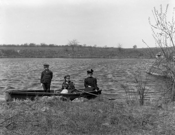 View from shoreline of Florentina, Jennie, and Edgar Krueger sitting in a rowboat on the quarry pond.