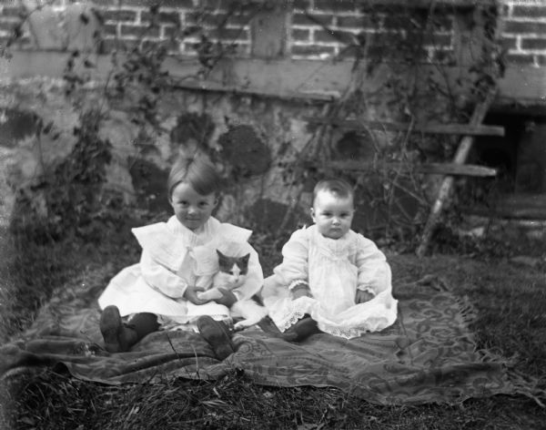 Ruth, holding a cat, and Alice Kressin sitting outdoors on a blanket. Behind them is the side of a half-timbered house.