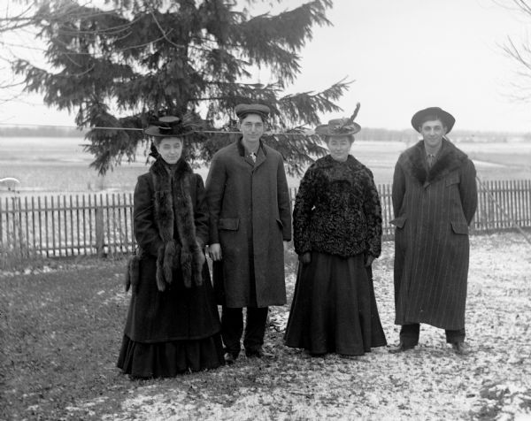 Emil Kuney's sister, Emil Kuney, Sarah Krueger, and Henry Bigalk standing outdoors in front of a fence during winter.
