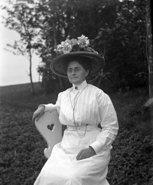 Outdoor portrait of Florentina Krueger sitting in a chair wearing a white dress and an elaborate hat.