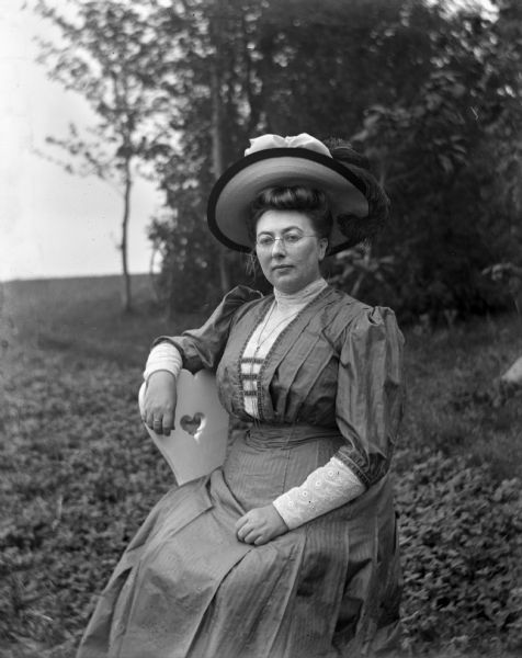 Outdoor portrait of Sarah Krueger sitting in a chair wearing a feathered hat.