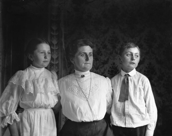 Indoor portrait of Florentina, Jennie, and Edgar Krueger. Florentina is sitting between the twins with an arm around each of their backs.