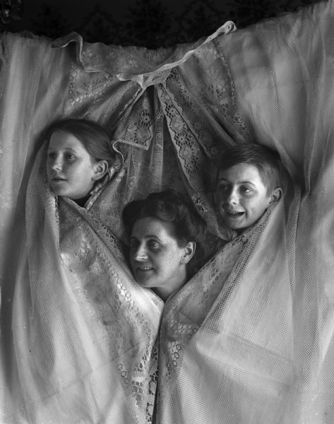 The family of photographer Alex Krueger posing playfully with their heads poking out of a curtain. From left to right are Jennie, Tina and Edgar.