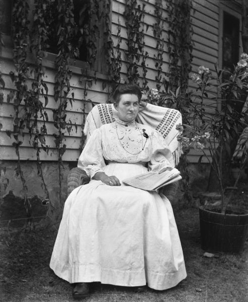 Tille Timmel, Florentina's cousin, sitting in a chair, outdoors, reading the newspaper. A large potted plant is sitting next to her.
