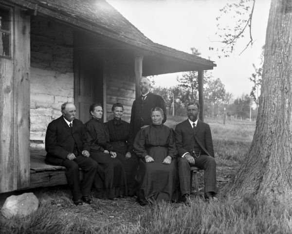 The six children of William Krueger posing on the front porch of their father's home, gathered for his funeral. From left to right, August, Amelia, Minnie, Albert (standing), Bertha and Henry Krueger.