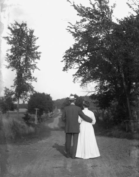 Rear view of Alexander and Florentina Krueger strolling down a road together. Alexander has his arm wrapped around Florentina's waist.