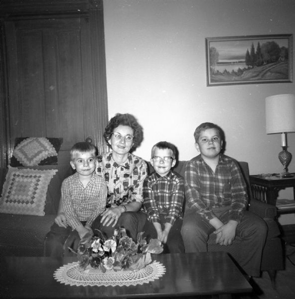 Shirley Krueger Oestreich sitting on a sofa in the living room with her three sons. From left to right: Dale, Shirley, Paul, and Glenn.