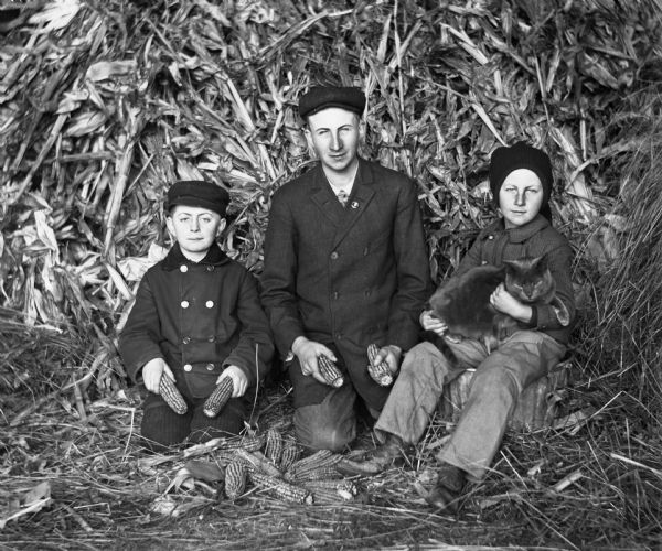 Edgar Krueger, Frank Albert Goetsch, and Anson Dewey Goetsch posing while husking corn on the Krueger farm.