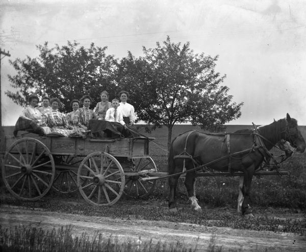Members of the Krueger family, including Edgar, Florentina, Jennie, and Sarah, sitting together in a lumber wagon on a Sunday ride. A two-horse team is pulling the wagon along the road.