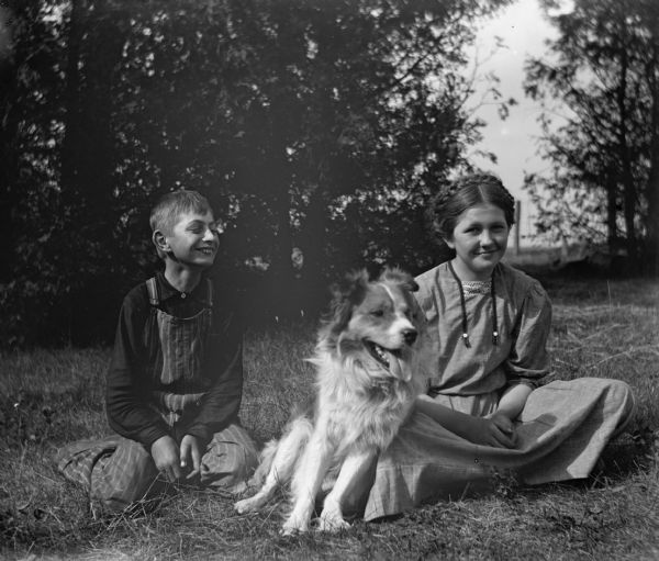 Edgar and Jennie Krueger sitting in the grass. A dog is sitting between them, leaning on Jennie's knee.