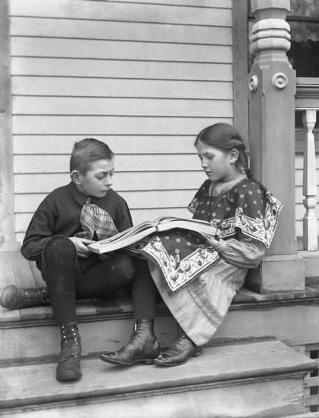 Twins Edgar and Jennie Krueger sitting on the steps of a porch reading a book together. They are nine-years-old.