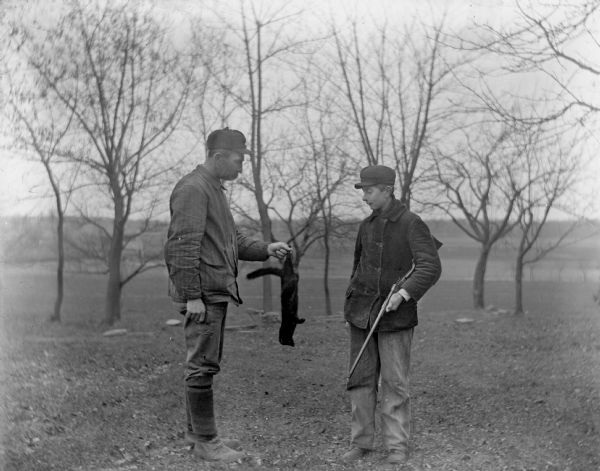 Alexander Krueger holding up a mink that Edgar Krueger trapped. Edgar is standing next to him looking at the mink while holding his rifle.