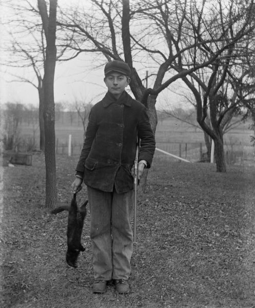 Young Edgar Kruegar holding a mink he trapped in one hand and a gun in the other.