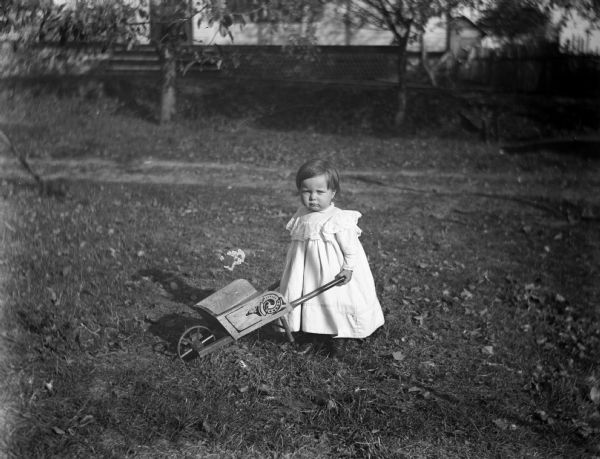 Eddie Wendorf as a baby pushing a toy wheelbarrow in a yard.