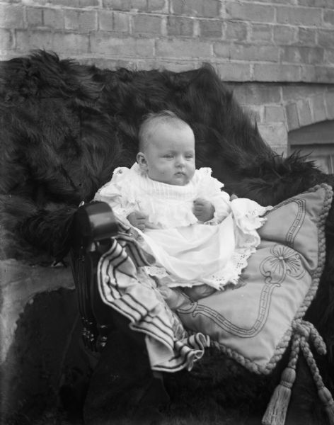Outdoor portrait of baby Viola Lettho propped up in a chair with two large pillows. The chair is covered with a fur blanket.