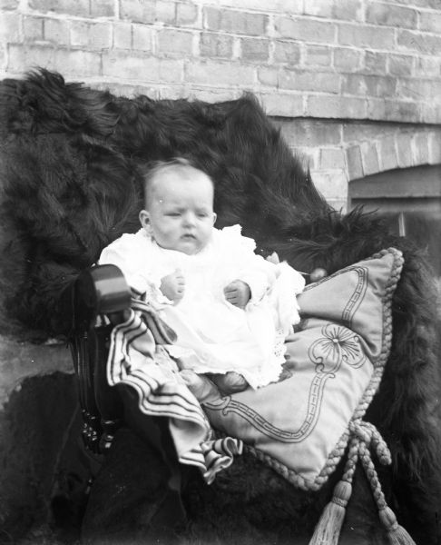 Outdoor portrait of baby Viola Lettho propped up in a chair with two large pillows. A fur blanket covers the chair.