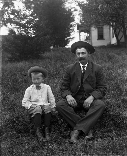 Outdoor portrait of Amandus Backhaus sitting in a yard with his son, Alex. A house is in the background.