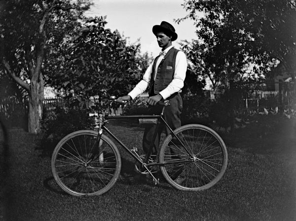 Therodore Miller standing and posing with his bicycle in a yard with a small garden.