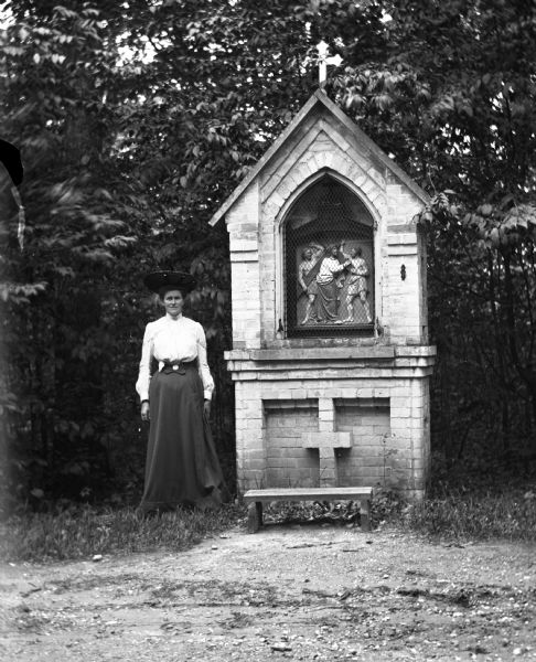Woman posing next to a pray station with a depiction of a station of the cross at Holy Hill.