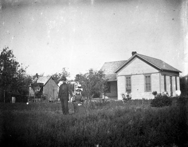 Edward Buenning and his wife posing in front of their home and farm buildings.