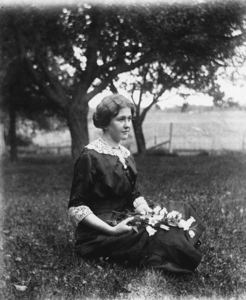 Outdoor portrait of Jennie Krueger sitting in the grass on the Krueger farm with a bouquet of flowers in her lap.