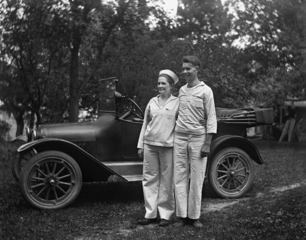 Jennie Krueger Bruetzman and her husband, Ernst Bruetzman, posing in white sailor uniforms in front of a 1917 Chevrolet.