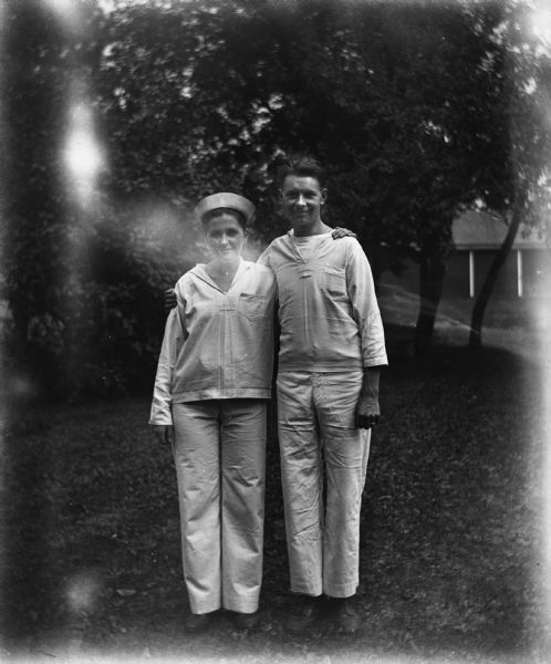 Outdoor portrait of Jennie Krueger Bruetzman and her husband, Ernst Bruetzman standing with their arms wrapped around each other in white sailor uniforms.