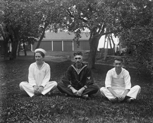Outdoor portrait of Jennie Krueger Bruetzman, Edgar Krueger, and Ernst Bruetzman sitting cross-legged on the lawn dressed in sailor uniforms. Jennie and Ernst are wearing white uniforms, while Edgar is dressed in a blue US Navy uniform.