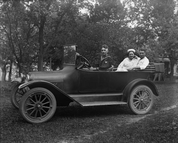 Edgar Krueger sitting in the drivers seat of a 1917 Chevrolet while Jennie Krueger Bruetzman and Ernst Bruetzman are sitting together in the back seat. All of them are wearing sailor uniforms.