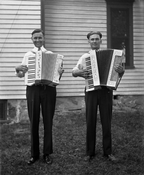 Ernst Bruetzman and Raymond Fehrmann playing accordions along the side of the Krueger home.