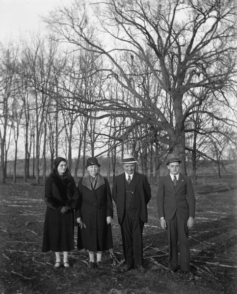 Outdoor portrait of the John Bhend family in front of a group of trees. From left to right, Irene, Sarah Krueger, John and Marcel Bhend.